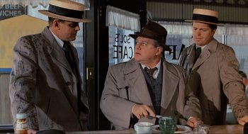 Movie still from “The Sting” (1973), directed by George Roy Hill – A man in a suit and hat sitting at a table with two other men; Medium shot, Over the shoulder angle