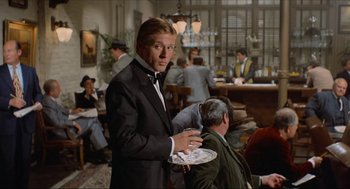 Movie still from “The Sting” (1973), directed by George Roy Hill – A man in a suit holding a tray in a room; Medium shot, Over the shoulder angle