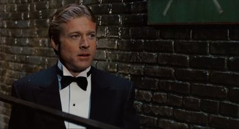 Movie still from “The Sting” (1973), directed by George Roy Hill – A man wearing a tuxedo and a bow tie in front of a brick wall; Close Up shot, Over the shoulder angle