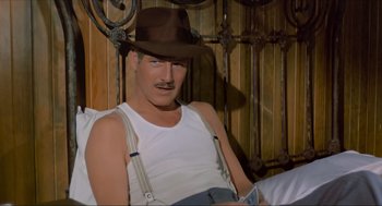 Movie still from “The Sting” (1973), directed by George Roy Hill – A man with a mustache wearing a brown hat and suspenders sitting on a bed; Medium shot, Low angle