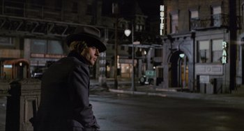 Movie still from “The Sting” (1973), directed by George Roy Hill – A man wearing a hat sitting on the side of the street; Wide shot, Over the shoulder angle