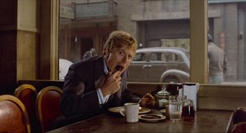 Movie still from “The Sting” (1973), directed by George Roy Hill – A man sitting at a table with a cup of coffee; Medium shot, Low angle