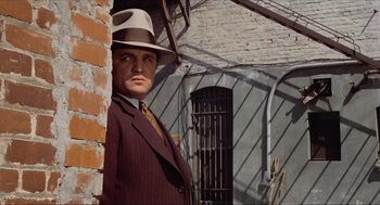 Movie still from “The Sting” (1973), directed by George Roy Hill – A man wearing a suit and hat standing next to a brick wall; Medium shot, Low angle