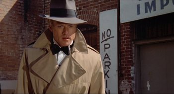 Movie still from “The Sting” (1973), directed by George Roy Hill – A man in a trench coat and hat standing in front of a no parking sign; Close Up shot, Low angle