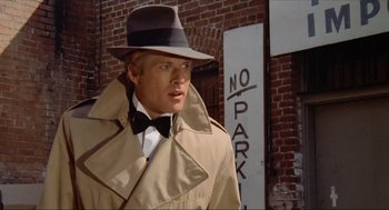 Movie still from “The Sting” (1973), directed by George Roy Hill – A man in a trench coat wearing a hat and a bow tie; Close Up shot, Low angle
