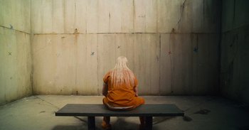 Movie still from “The Suicide Squad” (2021), directed by James Gunn – A person sitting on top of a wooden bench; Wide shot, High angle