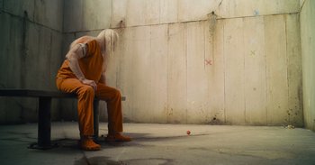 Movie still from “The Suicide Squad” (2021), directed by James Gunn – A man in orange is sitting on a bench; Wide shot, High angle