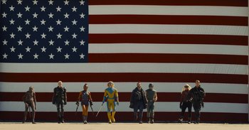 Movie still from “The Suicide Squad” (2021), directed by James Gunn – A group of people standing in front of an american flag; Wide shot, Low angle