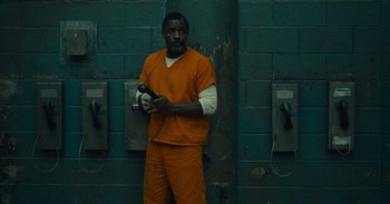 Movie still from “The Suicide Squad” (2021), directed by James Gunn – A man in an orange prison uniform standing in front of a phone booth; Wide shot, High angle