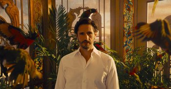 Movie still from “The Suicide Squad” (2021), directed by James Gunn – A man standing in front of a window with a bird perched on top of it; Medium shot, Low angle