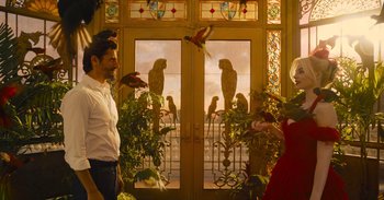 Movie still from “The Suicide Squad” (2021), directed by James Gunn – A man and a woman standing in front of a balcony with parakeets; Wide shot, Low angle
