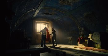 Movie still from “The Suicide Squad” (2021), directed by James Gunn – Two men are standing in a dimly - lit room; Wide shot, Low angle