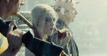 Movie still from “The Suicide Squad” (2021), directed by James Gunn – A woman holding an apple in front of a man holding an umbrella; Close Up shot, Over the shoulder angle
