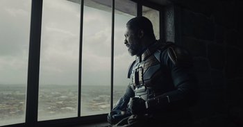 Movie still from “The Suicide Squad” (2021), directed by James Gunn – A man sitting in front of a window looking out at the sky; Medium shot, Low angle