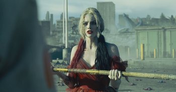 Movie still from “The Suicide Squad” (2021), directed by James Gunn – A woman holding a baseball bat while standing in a field; Medium shot, Over the shoulder angle