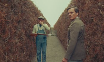 Movie still from “The Swan” (2023), directed by Wes Anderson – Two men standing next to each other on a dirt path; Wide shot, Over the shoulder angle