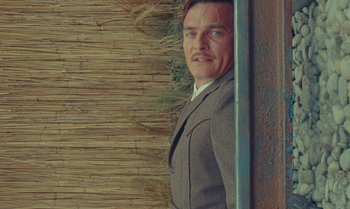 Movie still from “The Swan” (2023), directed by Wes Anderson – A man standing next to a wooden wall; Close Up shot, Low angle