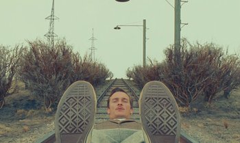 Movie still from “The Swan” (2023), directed by Wes Anderson – A man laying on the ground on a train track; Medium shot, Low angle