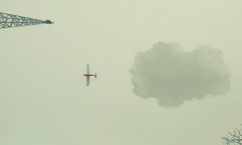 Movie still from “The Swan” (2023), directed by Wes Anderson – Two airplanes flying in the sky with a cloud behind them; Extreme Wide shot, Low angle