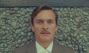 Movie still from “The Swan” (2023), directed by Wes Anderson – A person wearing a suit and tie; Close Up shot, High angle