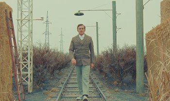 Movie still from “The Swan” (2023), directed by Wes Anderson – A man is standing on a train track; Wide shot, Low angle