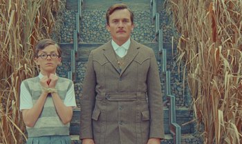 Movie still from “The Swan” (2023), directed by Wes Anderson – A man in a suit standing next to a woman in glasses; Medium shot, Low angle