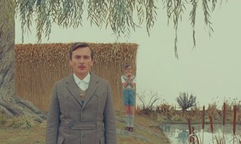 Movie still from “The Swan” (2023), directed by Wes Anderson – A man and a boy standing next to each other in a field; Medium shot, Low angle