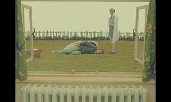 Movie still from “The Swan” (2023), directed by Wes Anderson – Two people are laying on the ground in the grass; Wide shot, Overhead angle