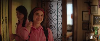 Movie still from “The Swimmers” (2022), directed by Sally El Hosaini – A woman in a pink shirt smiling for the camera; Close Up shot, Over the shoulder angle