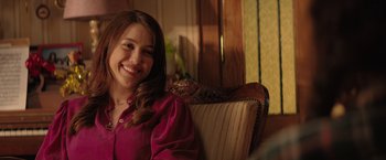 Movie still from “The Swimmers” (2022), directed by Sally El Hosaini – A woman sitting in a chair smiling for the camera; Close Up shot, Over the shoulder angle