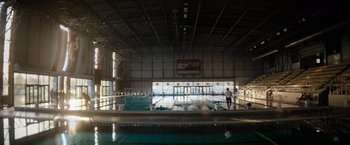 Movie still from “The Swimmers” (2022), directed by Sally El Hosaini – A man standing in front of an empty swimming pool; Extreme Wide shot, High angle