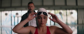 Movie still from “The Swimmers” (2022), directed by Sally El Hosaini – A woman wearing a swim cap and swimming goggles; Close Up shot, Over the shoulder angle