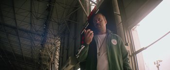 Movie still from “The Swimmers” (2022), directed by Sally El Hosaini – A man holding a baseball bat while standing in front of a building; Medium shot, Low angle
