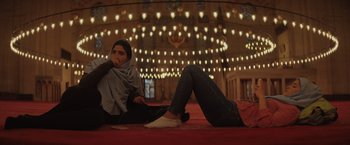 Movie still from “The Swimmers” (2022), directed by Sally El Hosaini – Two women sitting on the ground in a mosque; Wide shot, Low angle