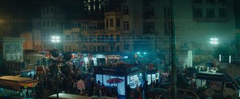 Movie still from “The Swimmers” (2022), directed by Sally El Hosaini – A crowd of people standing around a street at night; Extreme Wide shot, High angle
