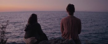 Movie still from “The Swimmers” (2022), directed by Sally El Hosaini – Two people sitting on a rock looking out at the ocean; Medium shot, Over the shoulder angle