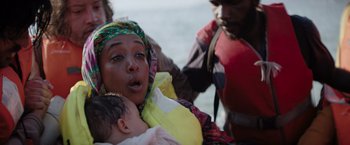 Movie still from “The Swimmers” (2022), directed by Sally El Hosaini – A woman holding a baby in her arms while a man looks on; Close Up shot, Over the shoulder angle