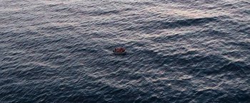 Movie still from “The Swimmers” (2022), directed by Sally El Hosaini – A small boat floating on top of a large body of water; Extreme Wide shot, Overhead angle