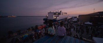 Movie still from “The Swimmers” (2022), directed by Sally El Hosaini – A group of people sitting next to a large boat; Extreme Wide shot, Low angle