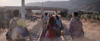 Movie still from “The Swimmers” (2022), directed by Sally El Hosaini – A group of people walking on train tracks near a bridge; Wide shot, Low angle