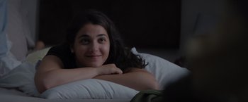 Movie still from “The Swimmers” (2022), directed by Sally El Hosaini – A woman laying in a bed smiling at the camera; Close Up shot, Over the shoulder angle