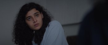Movie still from “The Swimmers” (2022), directed by Sally El Hosaini – A woman with a piercing is sitting in a room; Close Up shot, Over the shoulder angle