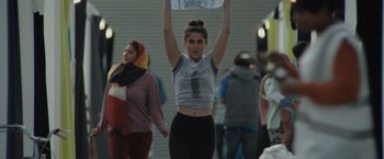 Movie still from “The Swimmers” (2022), directed by Sally El Hosaini – A woman is holding up a sign in the street; Medium shot, Low angle