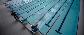 Movie still from “The Swimmers” (2022), directed by Sally El Hosaini – A person in a swimming pool on a bench; Wide shot, High angle