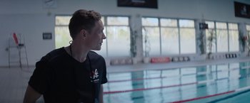 Movie still from “The Swimmers” (2022), directed by Sally El Hosaini – A man in black shirt standing in front of a pool; Medium shot, Over the shoulder angle