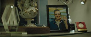 Movie still from “The Swimmers” (2022), directed by Sally El Hosaini – A picture of a man in a blue jacket is in front of a vase and a mirror; Extreme Close Up shot, High angle
