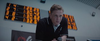 Movie still from “The Swimmers” (2022), directed by Sally El Hosaini – A man in a black and white shirt is holding a microphone; Close Up shot, Low angle