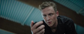 Movie still from “The Swimmers” (2022), directed by Sally El Hosaini – A man holding a cell phone in his hand; Close Up shot, Low angle