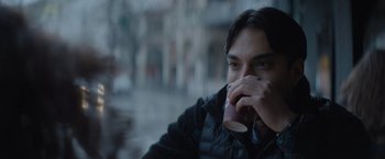 Movie still from “The Swimmers” (2022), directed by Sally El Hosaini – A man drinking a cup of coffee while sitting in a chair; Close Up shot, Over the shoulder angle