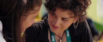 Movie still from “The Swimmers” (2022), directed by Sally El Hosaini – A woman wearing a lanyard talking to another person; Close Up shot, Over the shoulder angle